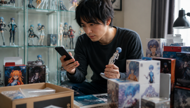 大量のフィギュアやアニメグッズを整理しながら買取サービスを比較検討している日本人の様子